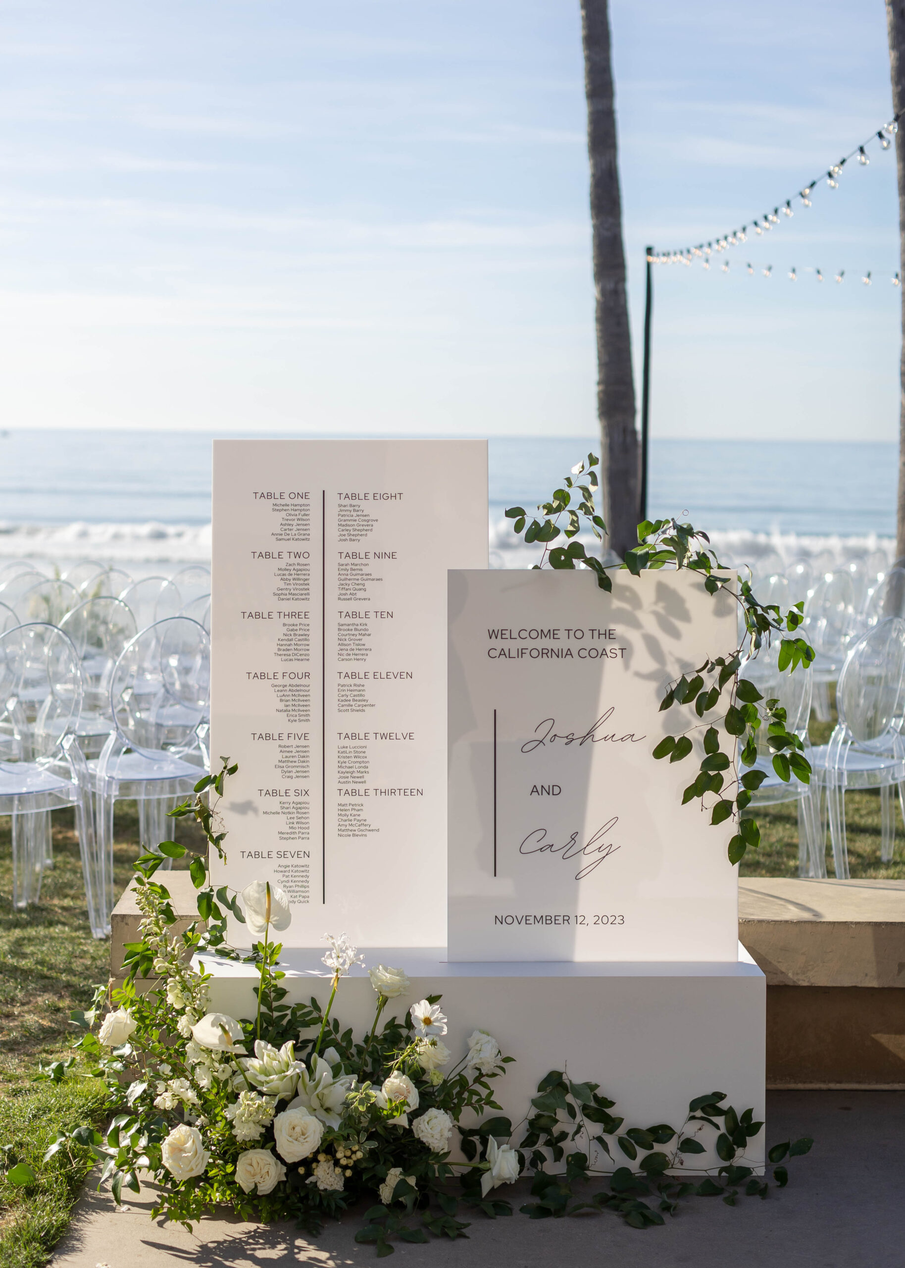 Beachside ceremony setup with clear chairs and white floral arch